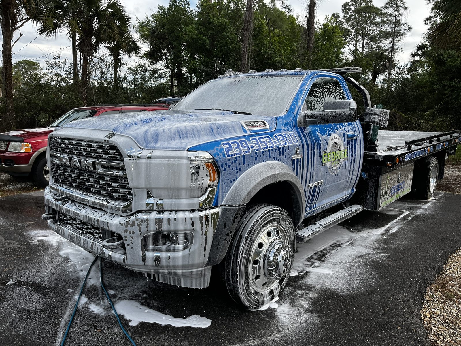 Wrapped flatbed tow truck under snow foam during an on-site fleet wash